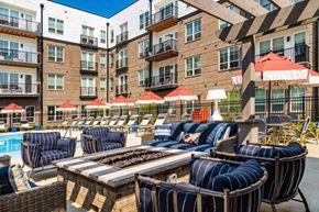 Lewis Center apartment for rent - A poolside area with lounge chairs and umbrellas in front of a multi-story apartment building.