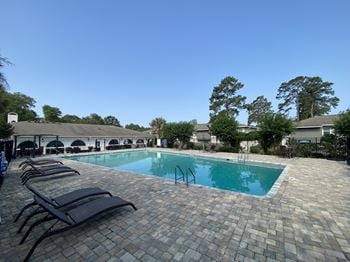 A swimming pool with chaise lounge chairs and trees in the background