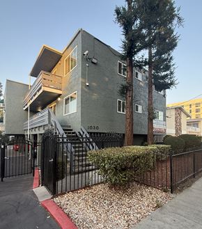San Jose apartment for rent - A grey building with a black fence and a red stripe on the sidewalk.