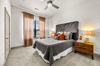 A bedroom with a large bed, a ceiling fan, and a window with curtains.