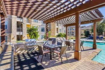 A patio with a table and chairs under a wooden pergola.