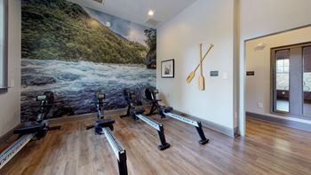 A row of exercise bikes in a room with a large painting on the wall