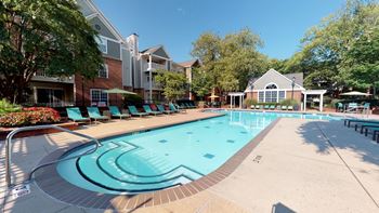A swimming pool with lounge chairs and umbrellas in front of a brick building