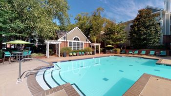A swimming pool with lounge chairs and umbrellas in front of a building