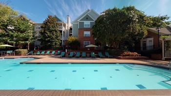 A swimming pool with lounge chairs and umbrellas in front of a brick building