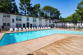 Memphis apartment for rent - A large swimming pool with a wooden deck and lounge chairs in front of a building. at Century Apartments, Memphis, TN, 38117