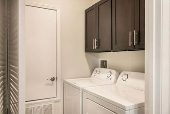A laundry room with white appliances and dark cabinets