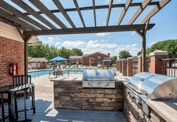 A patio with a grill and a swimming pool with umbrellas