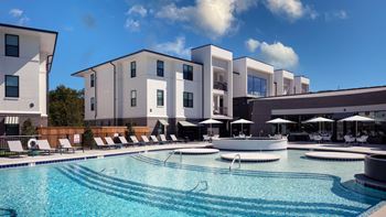 A large swimming pool with lounge chairs and umbrellas in front of a building