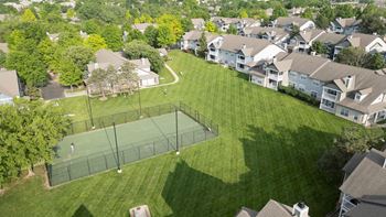 A tennis court is surrounded by houses and trees.