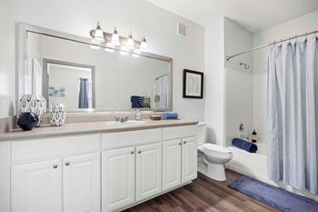 A bathroom with a white cabinet, a toilet, a sink, a mirror, and a shower.