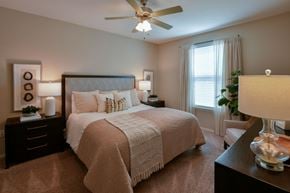 Arlington apartment for rent - A bedroom with a large bed, a ceiling fan, and a nightstand with a lamp. at Hall Creek Apartment Homes, Arlington 38002