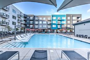 Memphis apartment for rent - A large outdoor swimming pool surrounded by lounge chairs and umbrellas at Highland Row Apartments, Memphis, Tennessee