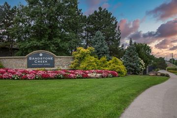 Overland Park apartment for rent - A sign for Sandstone Creek Apartment Homes is surrounded by flowers and greenery.