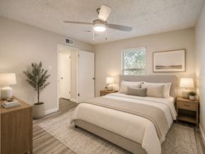 Irving townhouse for rent - A bedroom with a large bed, a ceiling fan, and a small tree.