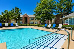 Broken Arrow apartment for rent - A swimming pool with a metal railing and blue water in front of a building with a red brick wall.