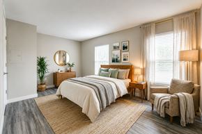 Broken Arrow apartment for rent - A bedroom with a large bed, a chair, and a plant.