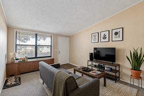 Louisville apartment for rent - A living room with a grey couch, a wooden entertainment center, and a large window.