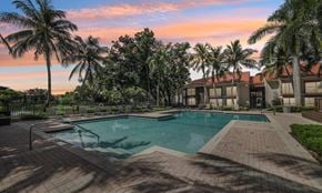 West Palm Beach apartment for rent - A swimming pool surrounded by palm trees and a building in the background.
