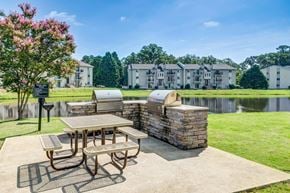 Fayetteville apartment for rent - A picnic table is set up in front of a stone wall with a lake and apartment buildings in the background.