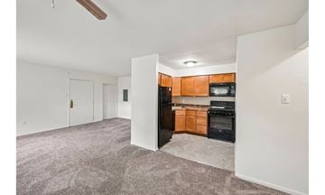 Allentown apartment for rent - A living room with a grey carpet and a kitchen area with wooden cabinets and black appliances.