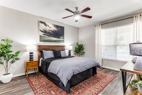 Austin apartment for rent - Dog-Friendly Apartments in North Austin, TX - Sycamore Springs - Furnished Bedroom with a Ceiling Fan, a Large Window, and Faux Plank Flooring