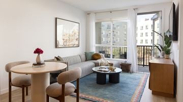 San Diego apartment for rent - A living room with a grey couch, a round table with a vase of flowers on it, and a television on the wall.
