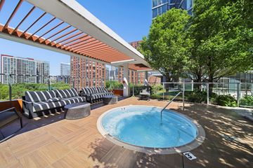 Chicago apartment for rent - A hot tub on a wooden deck with a striped couch and trees in the background.