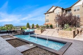 Wheat Ridge apartment for rent - A large outdoor swimming pool with a waterfall and a patio area with chairs and a table.