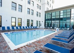 Portsmouth apartment for rent - A pool surrounded by blue chairs and a white building in the background.