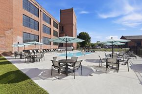 Martinsburg apartment for rent - A pool area with chairs and umbrellas in front of a brick building.