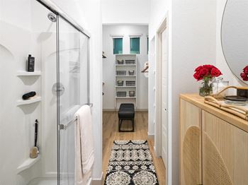 A bathroom with a glass shower door, a mirror, and a wooden vanity with a vase of red roses.