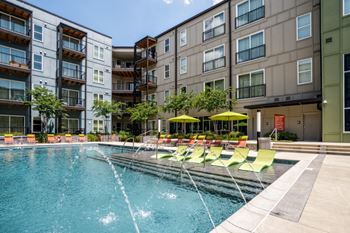 A swimming pool with yellow and green chairs in front of an apartment building