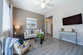Surprise apartment for rent - A living room with a couch, a chair, a coffee table, and a flat-screen TV mounted on the wall at Vistoria At Marley Park Apartments, Surprise, AZ, 85379