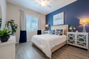Surprise apartment for rent - A bedroom with a bed, nightstand, and a plant. at Vistoria At Marley Park Apartments, Arizona