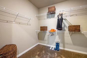 A room with a carpeted floor and a wall-mounted shelf with baskets and a hanging garment.