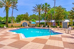 Palm Coast apartment for rent - A large outdoor swimming pool surrounded by palm trees and lounge chairs.