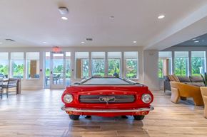 Mount Dora apartment for rent - A red vintage car is parked in a spacious room with wooden floors and large windows.