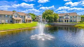 Kissimmee apartment for rent - A fountain in the middle of a pond in front of apartment buildings.