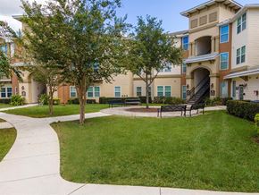Kissimmee apartment for rent - a grassy area with benches and trees in front of an apartment building