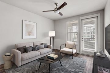 Arvada apartment for rent - A living room with a grey couch, a black coffee table, a white chair, a ceiling fan, and a painting on the wall.