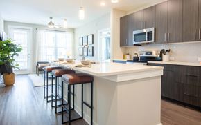 Atlanta apartment for rent - Kitchen island with white quartz, three leather counter stools, dark woodgrain cabinets, and stainless appliances.
