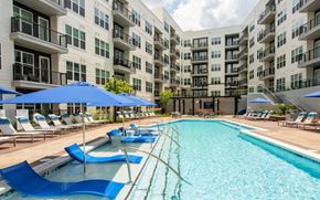 Atlanta apartment for rent - Pool with blue in-water loungers on a shelf, handrails, blue shade umbrellas, and balcony wings behind the deck.