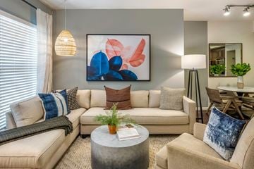 Pembroke Pines apartment for rent - A living room with a large abstract painting on the wall, a beige sofa, a grey coffee table, and a dining table with chairs.