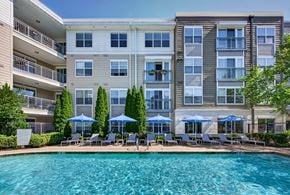 Swampscott apartment for rent - Pool and sun deck lined with blue umbrellas and gray loungers, below apartment balconies and tall arborvitae hedges.