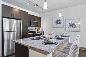 Swampscott apartment for rent - Kitchen with a speckled granite island seating three, dark cabinets, stainless appliances and track lighting above.