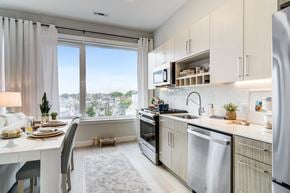 Revere apartment for rent - Galley kitchen with pale cabinets, a gas range and quartz counters, beside a dining table set at the wide window.