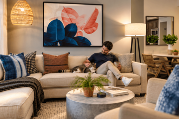 Pembroke Pines apartment for rent - A man is sitting on a couch in a living room with a large abstract painting on the wall behind him.