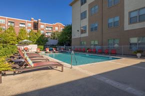 Dallas apartment for rent - A pool area with chairs and umbrellas in front of a building.