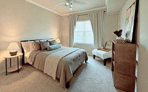 Dallas apartment for rent - A bedroom with a large bed and a small table with a lamp on it.